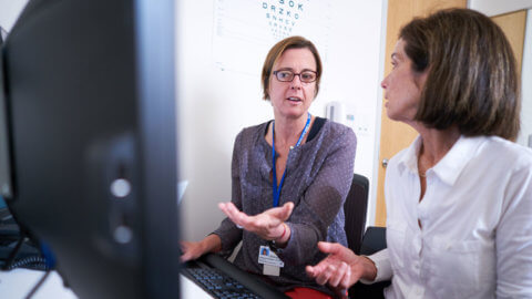 Print Journal Cancellations, two UCSF staff members talking and using a desktop