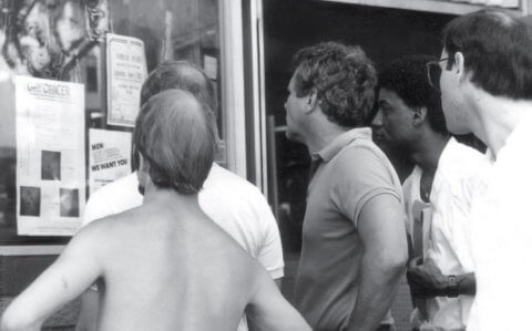 Black-and-white of five men looking at a flyer with the title "gay cancer."