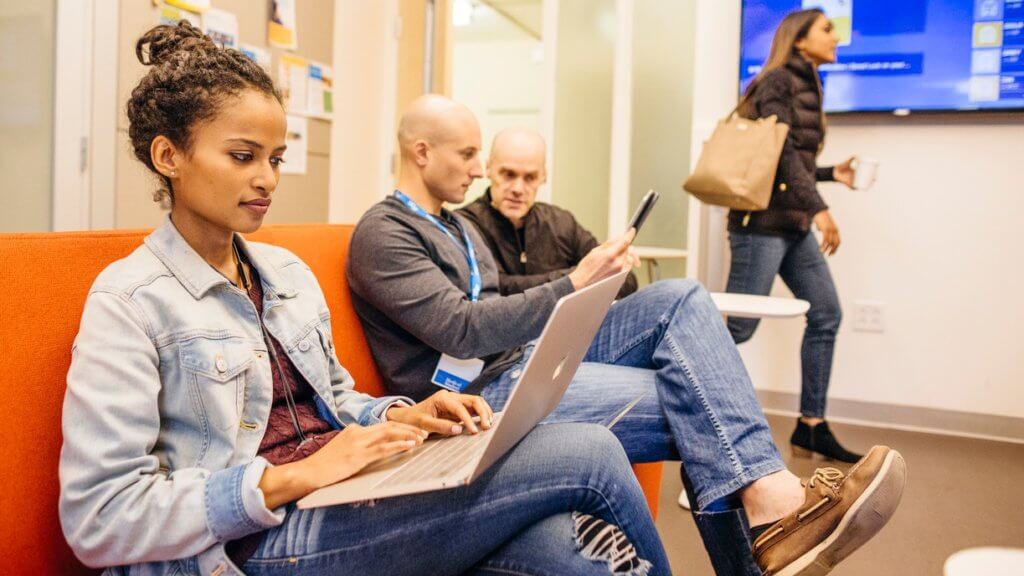 three people sitting working on a sofa