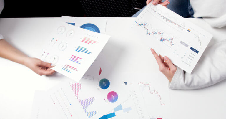 Two sets of hands holding print outs of colorful graphs and charts