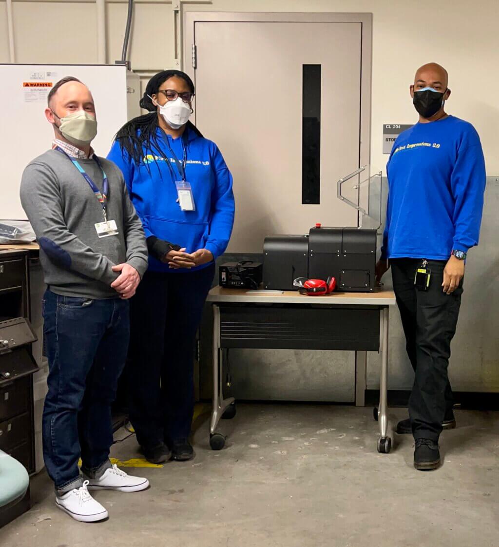 Three people standing next to 3D printed filament shredder.