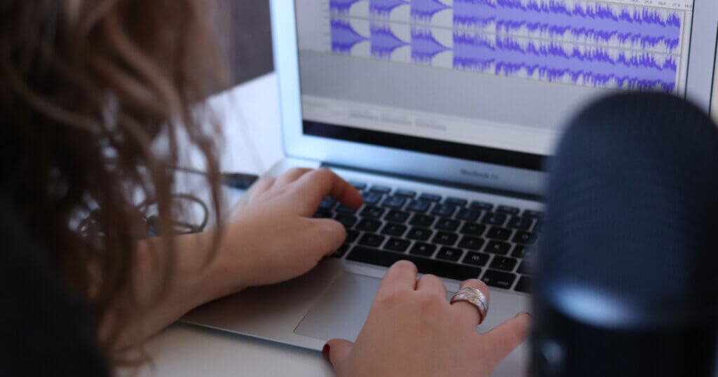 Person editing an audio file on a laptop, in the foreground is a microphone.