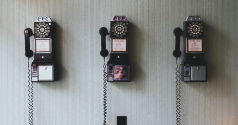 Three black rotary phones on a wall.