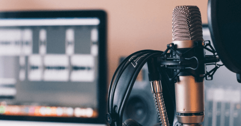 Professional recording microphone and headphones with an out of focus monitor in the background showing audio files.