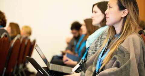 Attendees listening while attending a conference and working on their laptops.