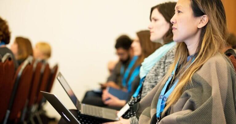 Attendees listening while attending a conference and working on their laptops.