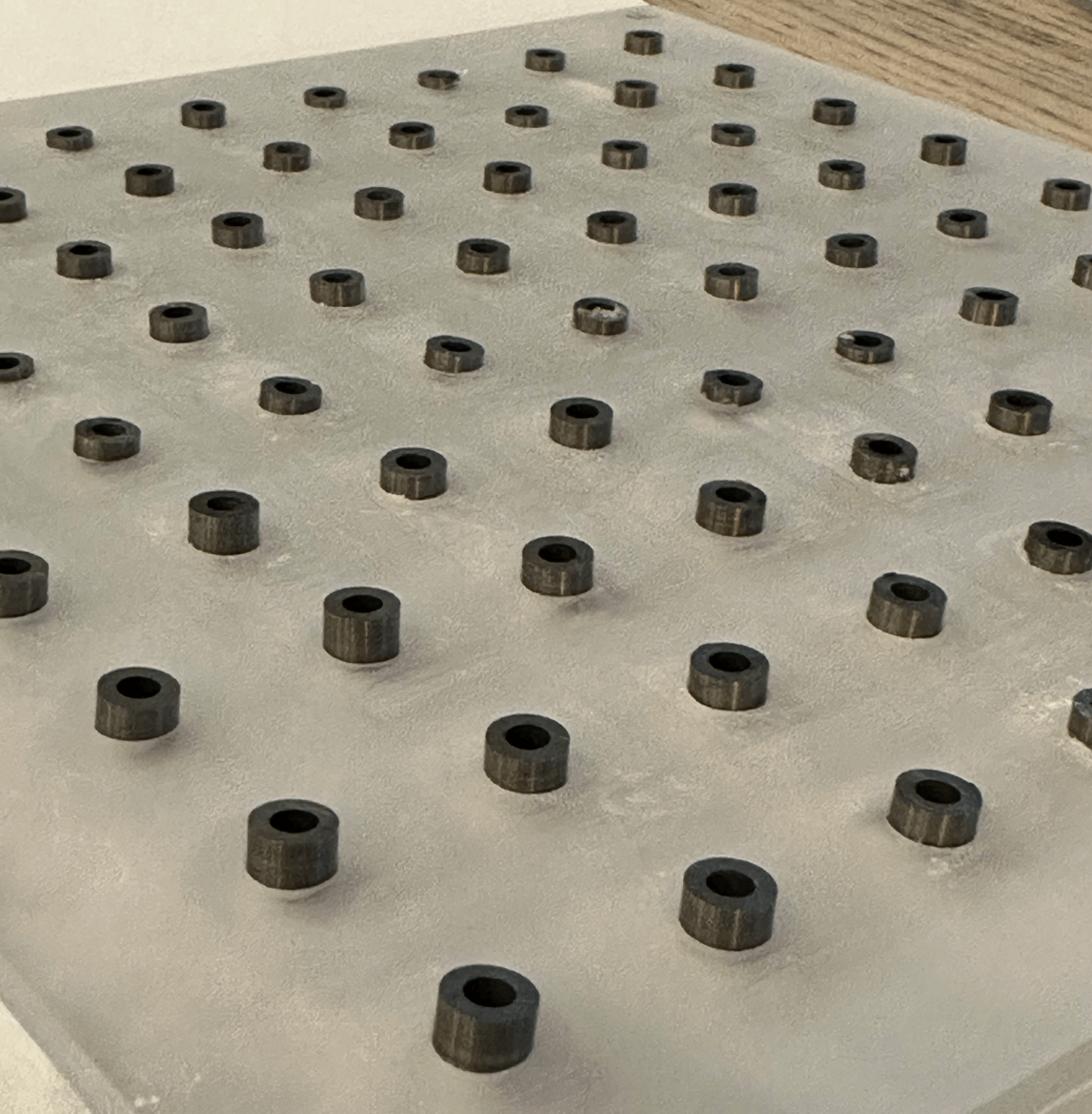 Picture of a clear 3D printed square grid with circular metal alloy segments inserted into each hole.