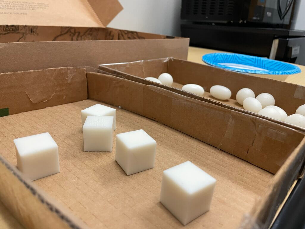 Close-up of white resin cubes and ellipsoids in cardboard trays