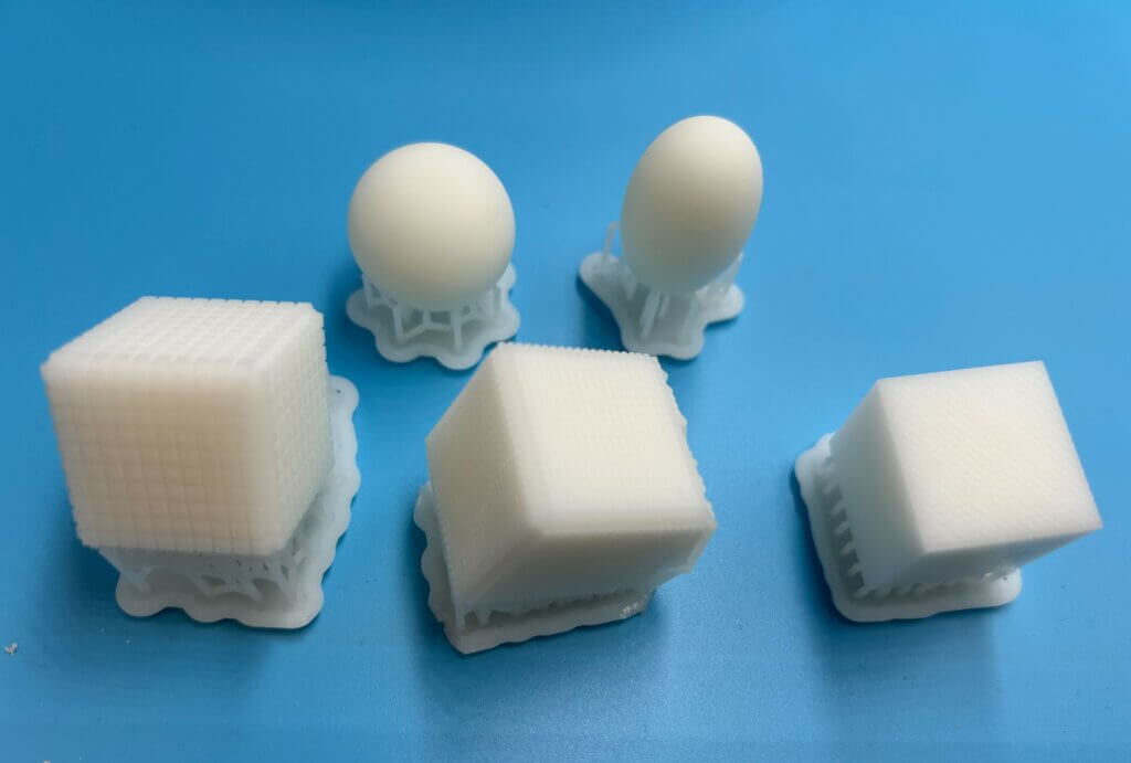 Various 3D printed shapes (cubes, ellipsoid and sphere) made from white resin on a blue background