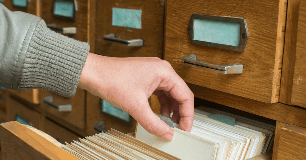 Hand reaching for an index card in a pulled out drawer.