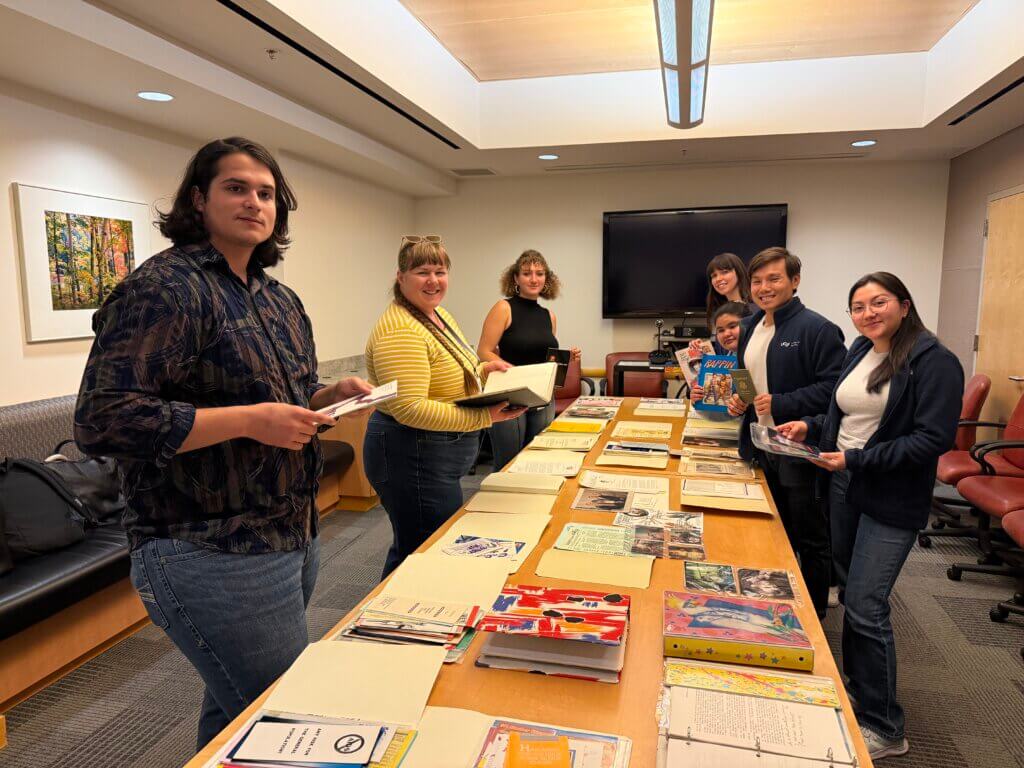 Seven people from CFAR are standing around a table, smiling and holding archival materials.
