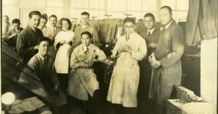 A group of UCSF dentistry students in lab coats inside a lab with tools and equipment.