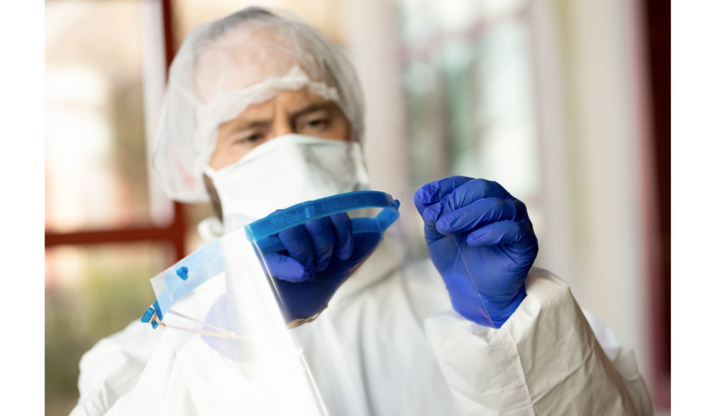 Person in protective gear holding a transparent face shield.
