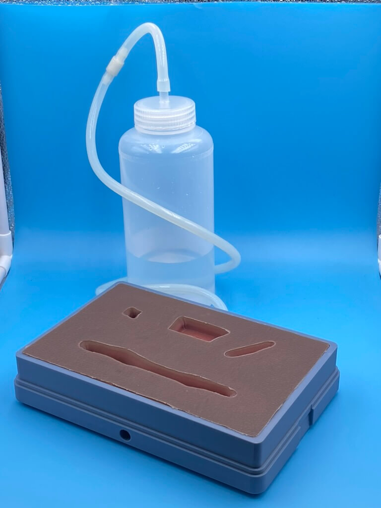 three images side-by-side of the bleed-control model which has flesh-toned silicon on top, two images have a clear bottle and tube to hold liquid.