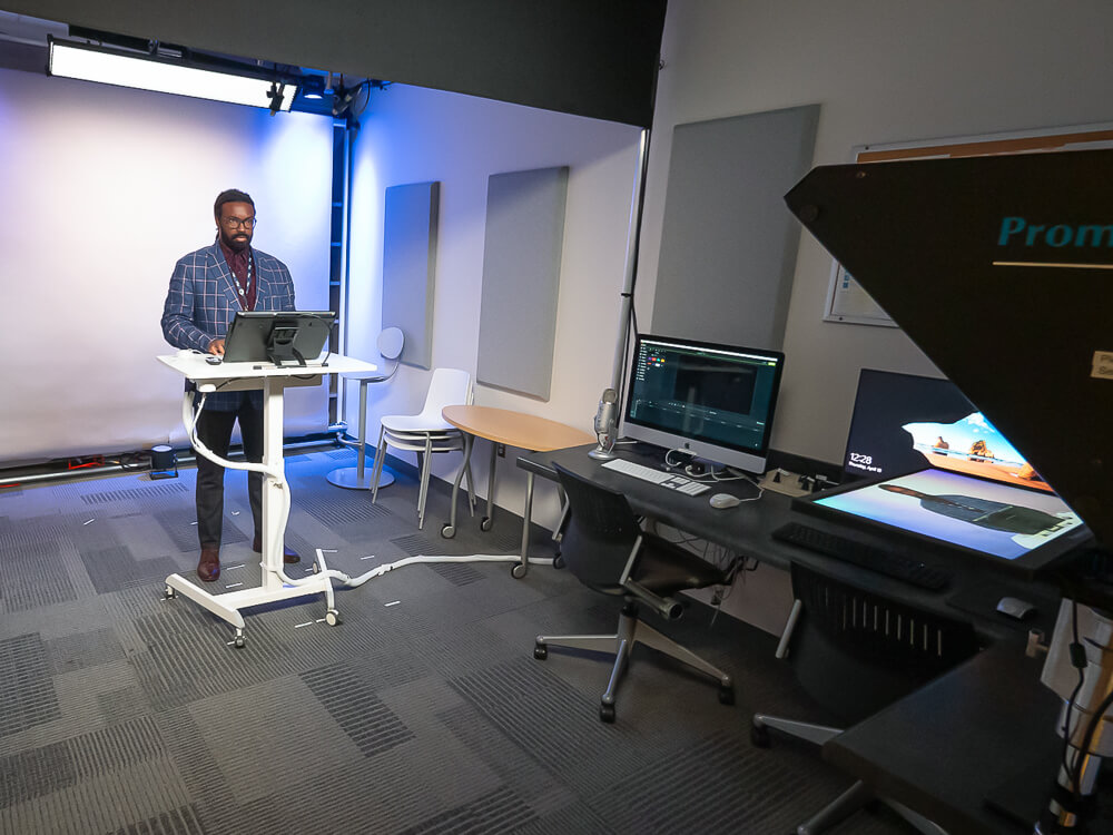 Joshua Cobbett, tech innovations specialist, standing at a podium and facing a teleprompter within the Library Recording Studio