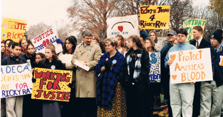 Dana Kuhn and Louise Ray in a crowd of high school students at a rally holding signs with slogans like "Vote Today 4 Ricky Ray" and "Protect America's Blood".