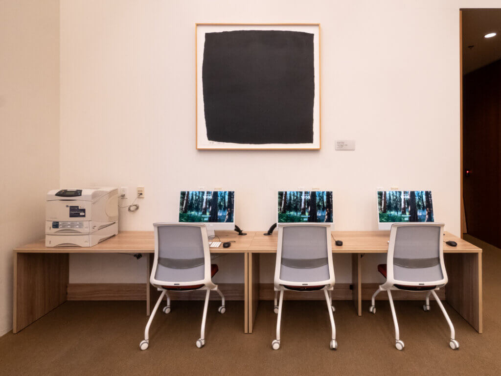 Three desktop stations with chairs and a printer on the left. 