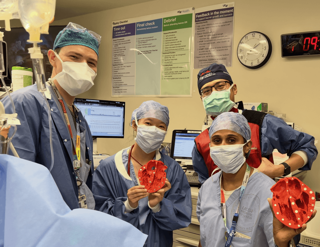 Dr. Litty John and three cardiovascular anesthesiology fellows in masks and scrubs holding up the 3D printed heart model used in the operating room (OR).