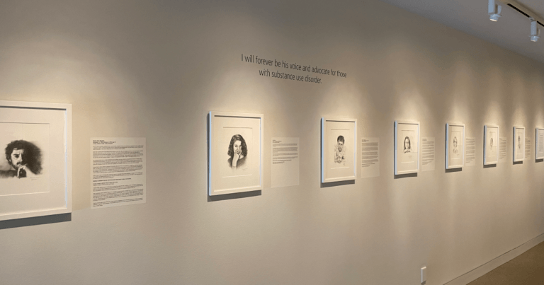 A large white wall with charcoal portraits and narratives on display